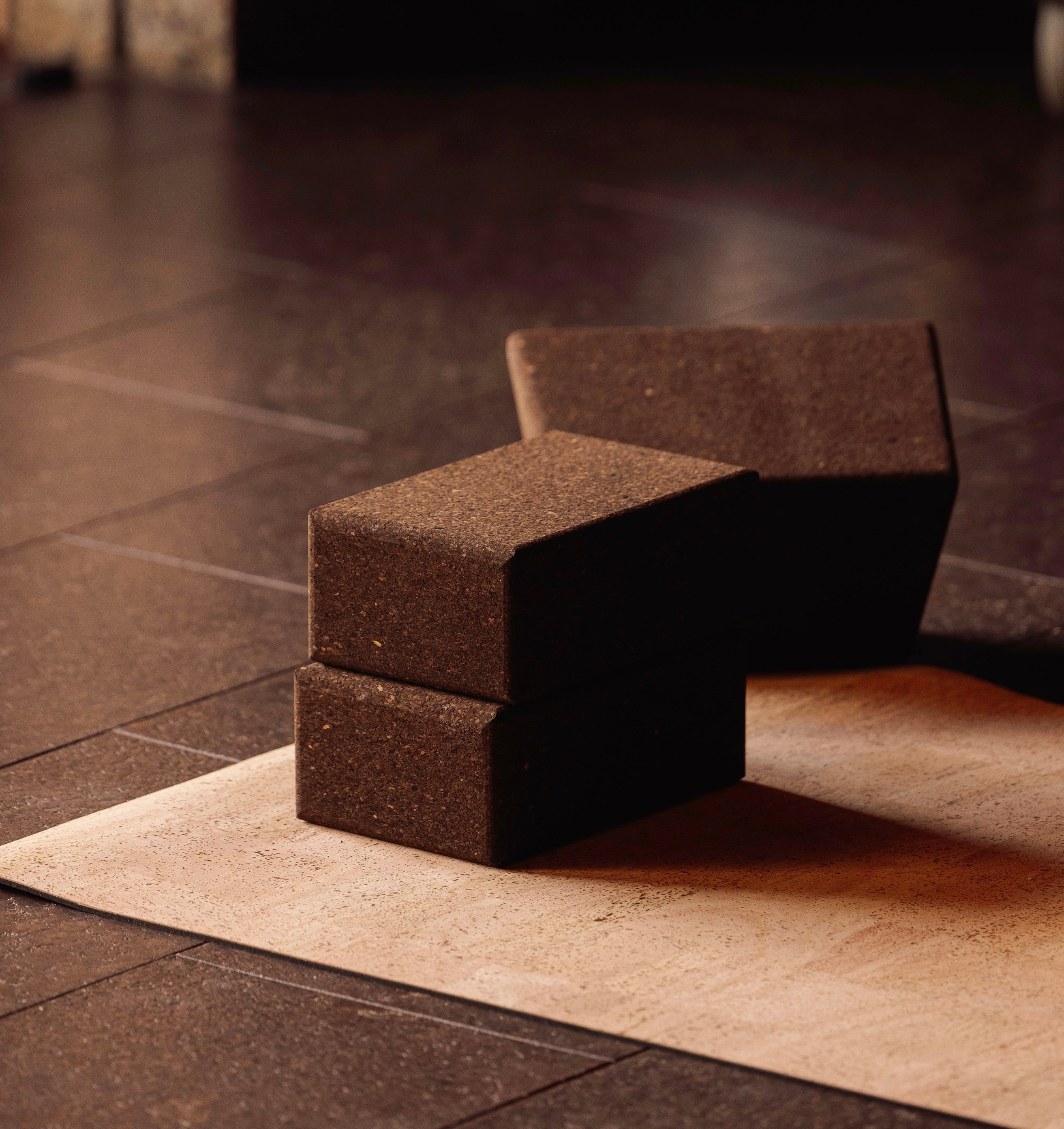 Two sustainable natural brown cork yoga blocks from Rituil, ideal for yoga and pilates practice and stretching exercises on a natural cork leather yoga mat on a dark tiled floor.