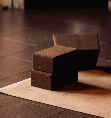 Two sustainable natural brown cork yoga blocks from Rituil, ideal for yoga and pilates practice and stretching exercises on a natural cork leather yoga mat on a dark tiled floor. #color_ash #color_earth
