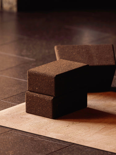Two sustainable natural brown cork yoga blocks from Rituil, ideal for yoga and pilates practice and stretching exercises on a natural cork leather yoga mat on a dark tiled floor. #color_ash #color_earth