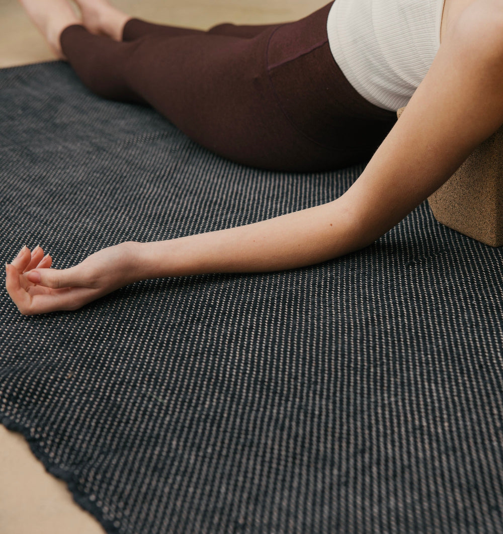 Woman practicing restorative yoga on ⁠heavyweight and oversized sustainable recycled cotton yoga rug on a studio floor, showcasing an extra-thick and extra-wide supportive texture