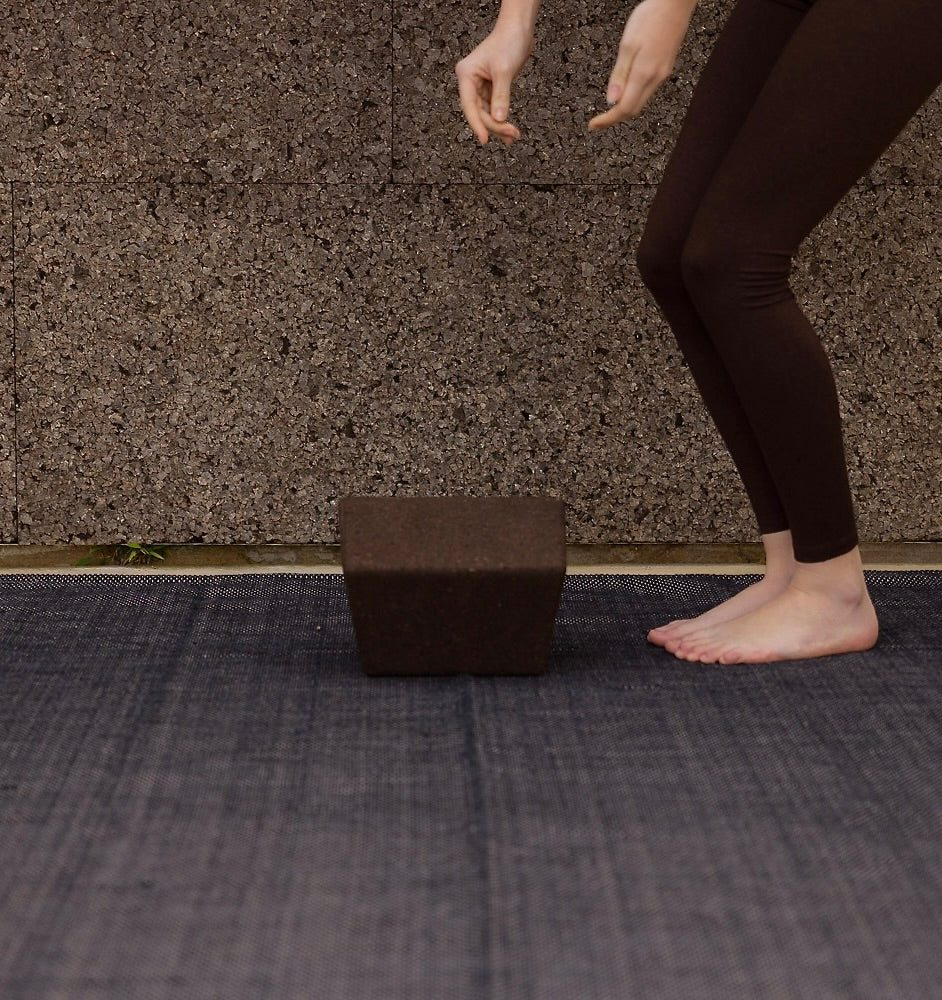 Woman placing sustainable Portuguese cork resotorative yoga and Pilates block on top of restorative cotton yoga rug.