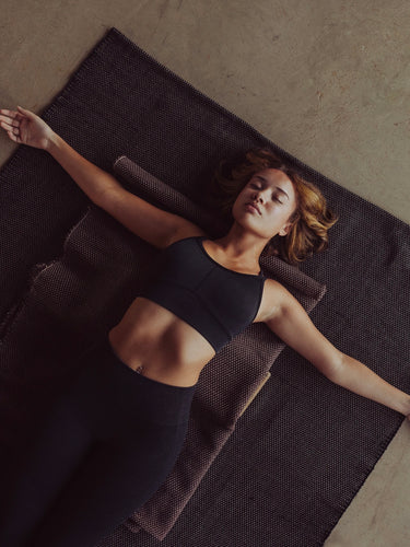 Woman practicing restorative yoga on ⁠heavyweight and oversized sustainable recycled cotton yoga rug on a studio floor, showcasing an extra-thick and extra-wide supportive texture