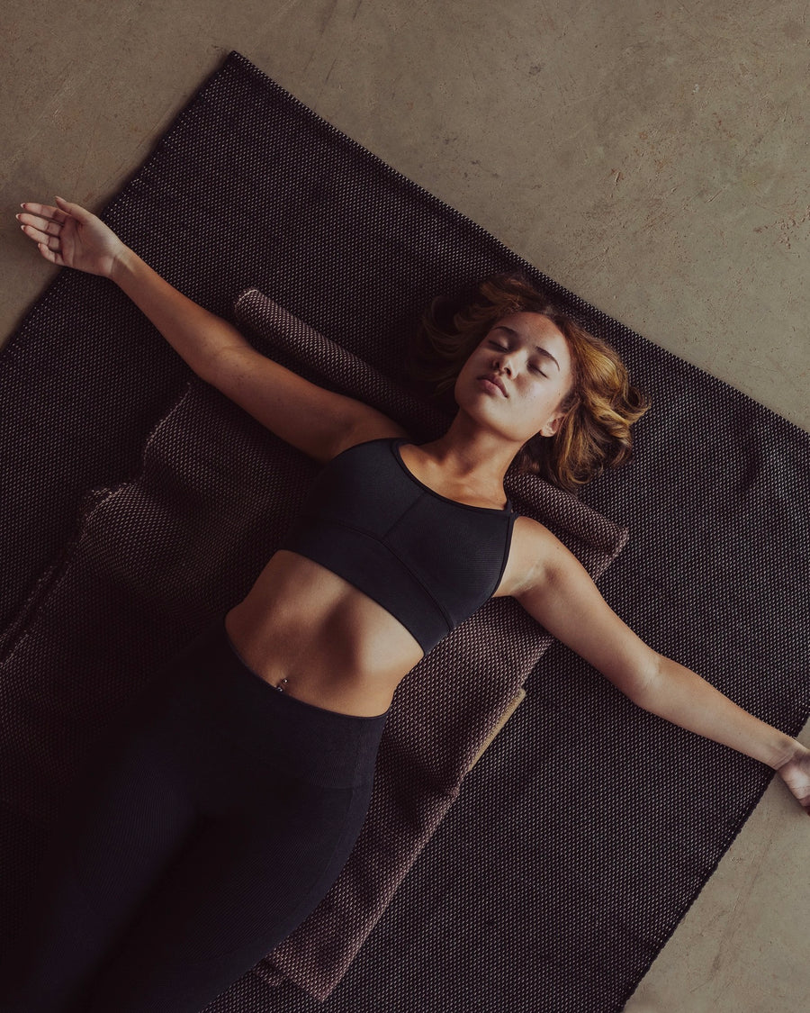Woman practicing restorative yoga on ⁠heavyweight and oversized sustainable recycled cotton yoga rug on a studio floor, showcasing an extra-thick and extra-wide supportive texture