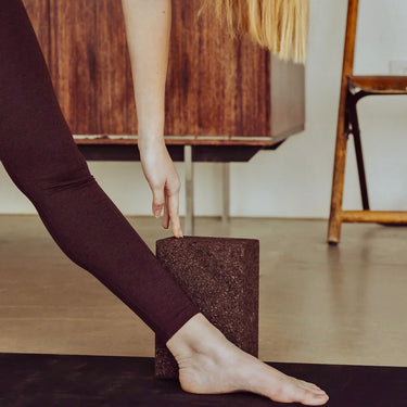 woman with hand on cork yoga block and foot on Rituil™ ash / black yoga mat #color_earth