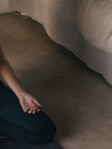 woman meditating on Rituil™ recycled cotton yoga rug in bedroom with linen bedding