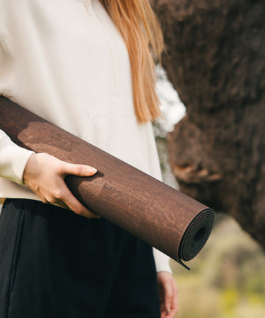 Woman holidng Rituil sustainable natural brown cork leather yoga mats featuring a non-slip, non-toxic cork surface in front of cork tree