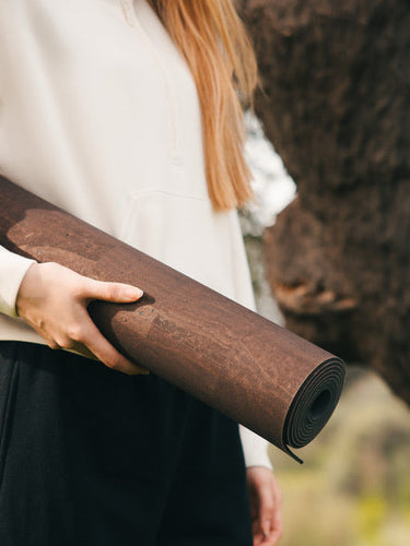 Woman holidng Rituil sustainable natural brown cork leather yoga mats featuring a non-slip, non-toxic cork surface in front of cork tree