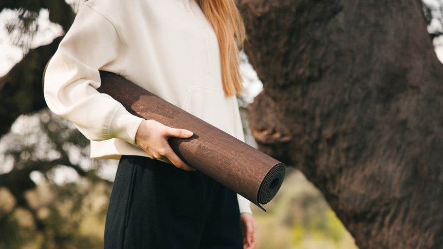 Woman holidng Rituil sustainable natural brown cork leather yoga mats featuring a non-slip, non-toxic cork surface in front of cork tree