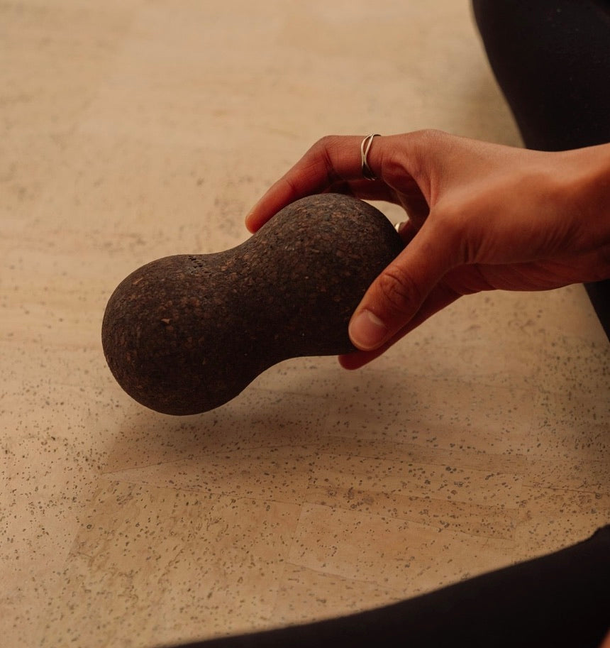 Rituil sustainable Portuguese cork massge peanut for yoga, Pilates core workouts, and deep tissue muscle recovery shown wiht womans hand pressing into peanut on cork yoga mat