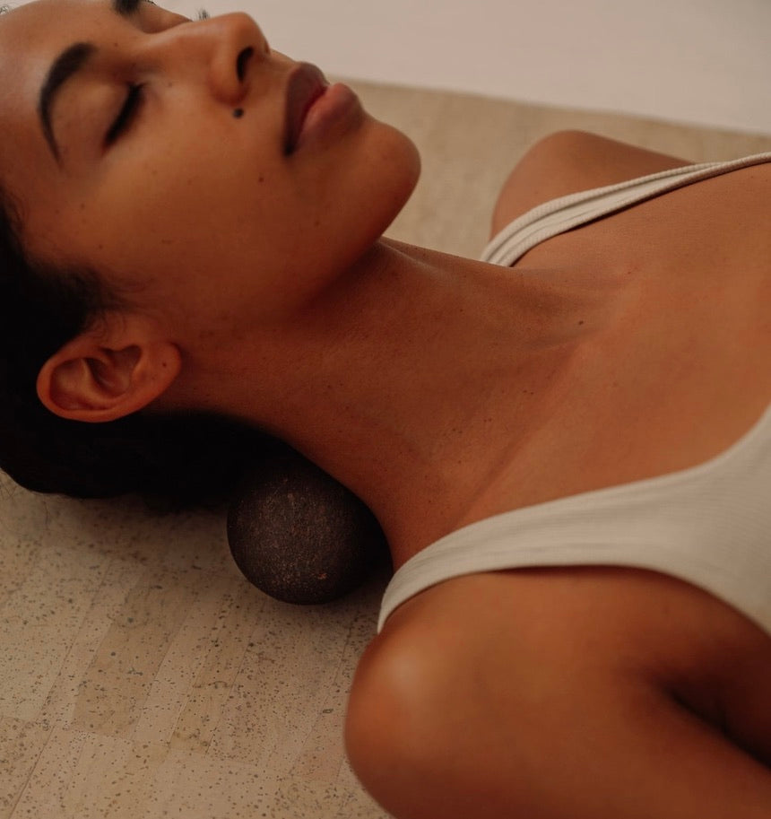 Woman massaging neck with Rituil sustainable Portuguese cork peanut while laying on cork yoga mat