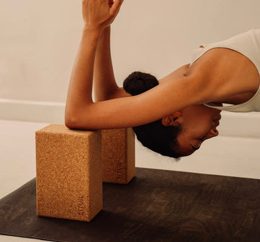 Rituil sustainable natural brown cork leather yoga mat featuring a non-slip, non-toxic, pvc free, with natural cork yoga blocks and woman practicing yoga 