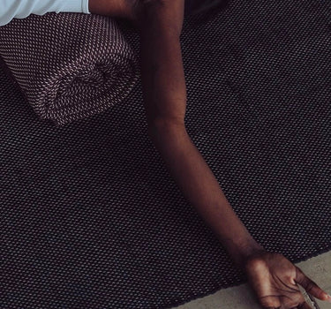 Woman practicing restorative yoga on ⁠heavyweight and oversized sustainable recycled cotton yoga rug on a studio floor, showcasing an extra-thick and extra-wide supportive texture #color_ash