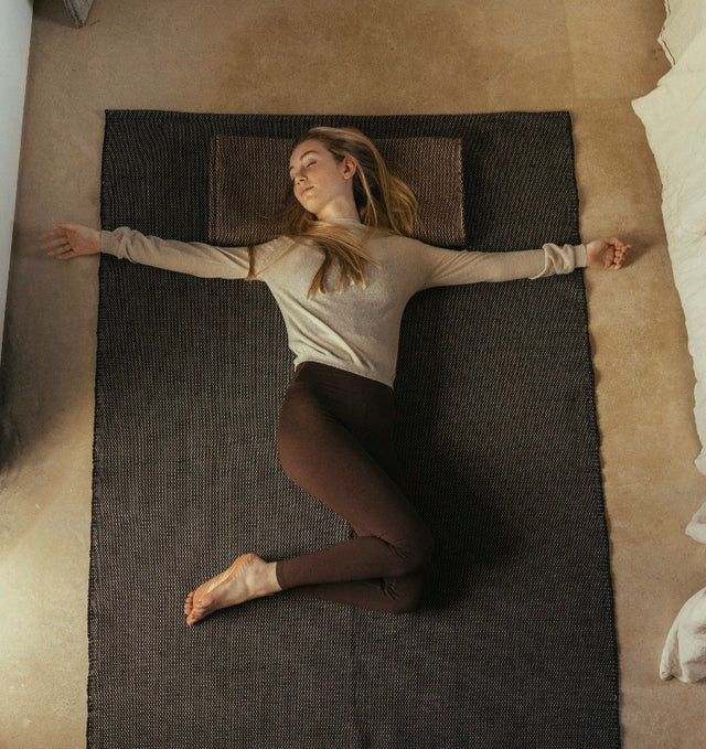 Woman practicing restorative yoga on recycled cotton yoga rug on a studio floor