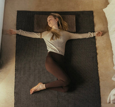 Woman practicing restorative yoga on recycled cotton yoga rug on a studio floor