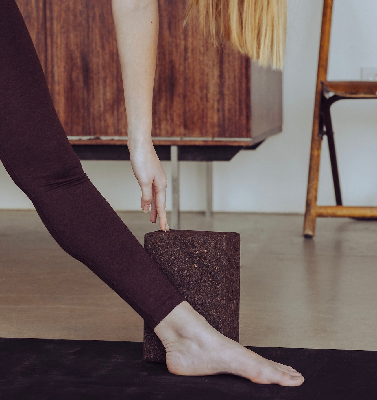 woman with hand on cork yoga block and foot on Rituil™ ash / black yoga mat #color_earth