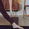 woman with hand on cork yoga block and foot on Rituil™ ash / black yoga mat #color_earth