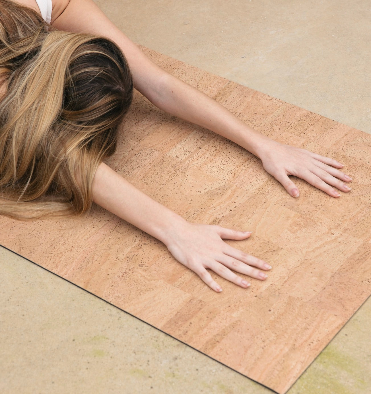 woman with hands in childs pose on sand or natural cork yoga mat #color_sand