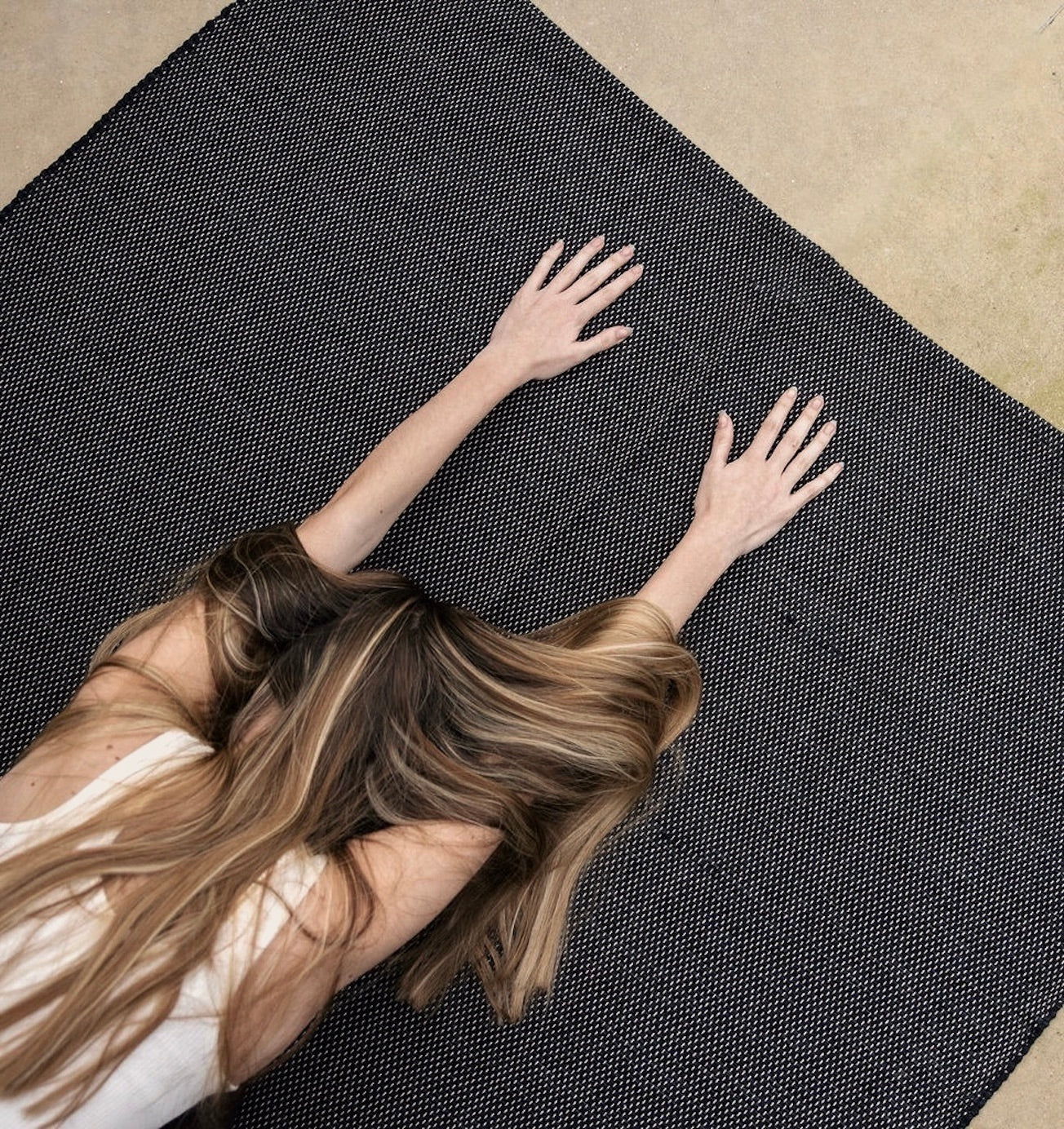woman in childs pose with hands on Rituil™ ash or black recycled cotton yoga rug #color_ash