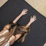 woman in childs pose with hands on Rituil™ ash or black recycled cotton yoga rug #color_ash