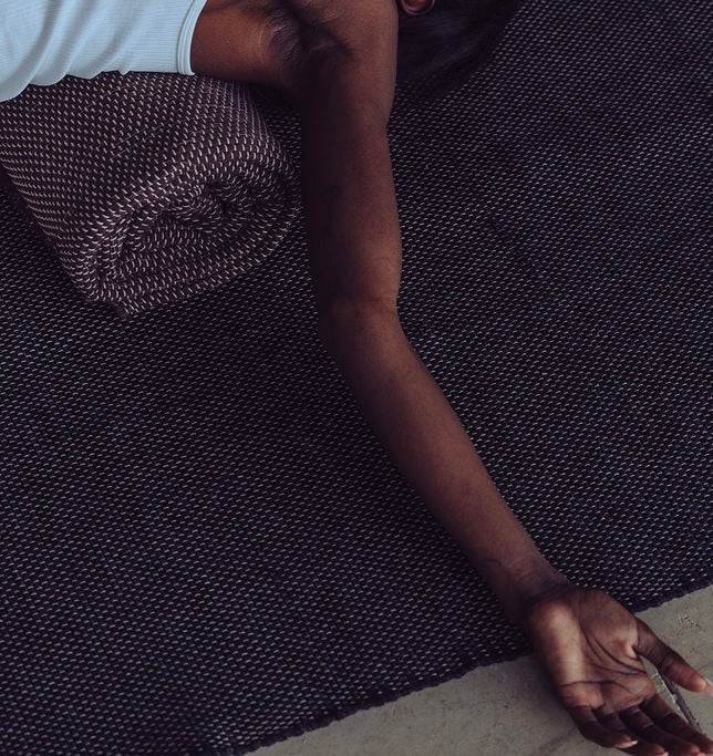 image of woman laying on rolled Rituil™ yoga recycled cotton rug in ash or black color #color_ash