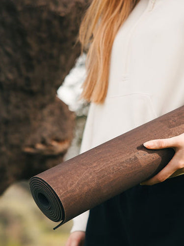 woman holding the Rituil™ cork yoga mat in earth color next to a cork tree