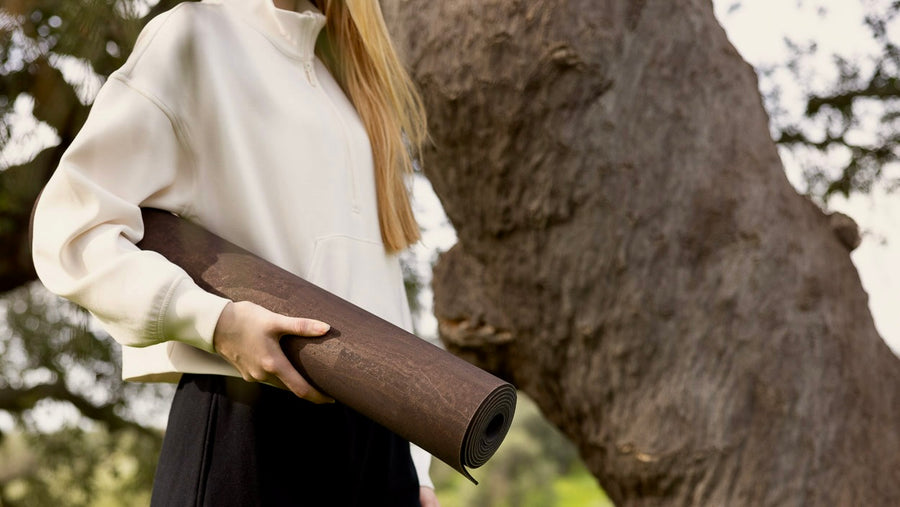 Person holding a cork mat rolled-up mat outdoors with trees in the background.