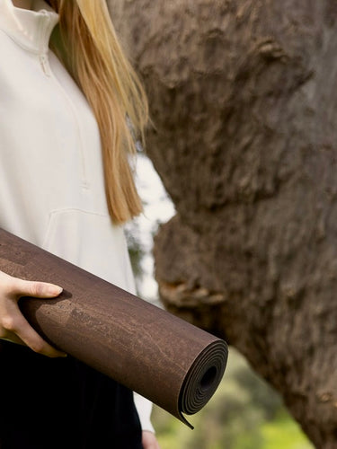 Person holding a cork mat rolled-up mat outdoors with trees in the background.