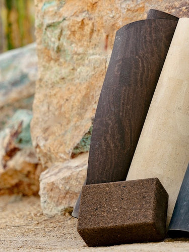 Rituil sustainable natural brown, cream and black cork leather yoga mats featuring a non-slip, non-toxic, pvc free surface rolled up and leaning on rock