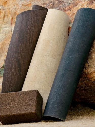 Rituil cork yoga mats and cork yoga block in earth, sand, and slate colors leaning against natural stone