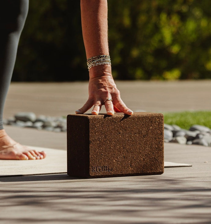 Person using a rituil cork yoga block on a wooden deck with a blurred natural background  #color_earth