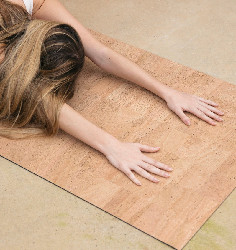 woman with hands in childs pose on sand or natural cork yoga mat