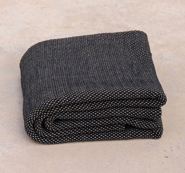 ⁠Heavyweight and oversized sustainable recycled cotton yoga rug in black folded on a studio floor, showcasing an extra-thick supportive texture