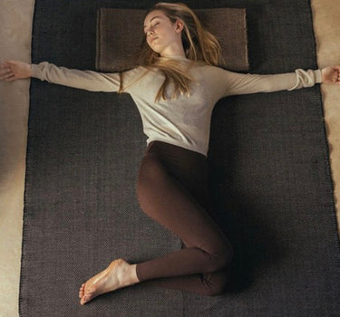 Woman practicing restorative yoga on ⁠heavyweight and oversized sustainable recycled cotton yoga rug on a studio floor, showcasing an extra-thick and extra-wide supportive texture #color_ash