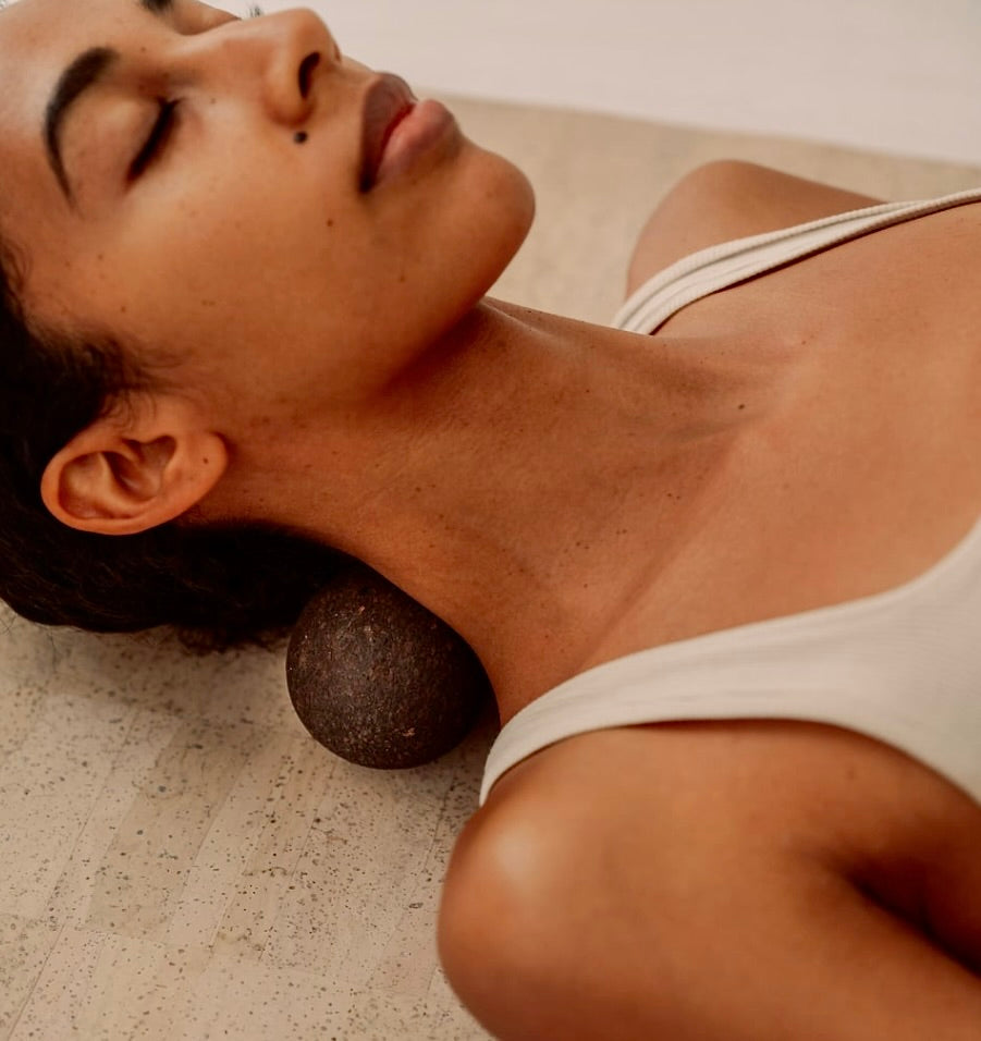 Woman massaging neck with Rituil sustainable Portuguese cork peanut while laying on cork yoga mat